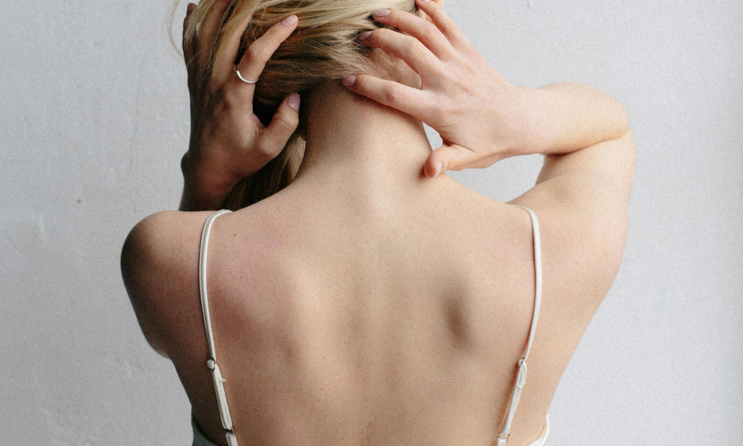 back view of woman in tank top holding her hair and neck