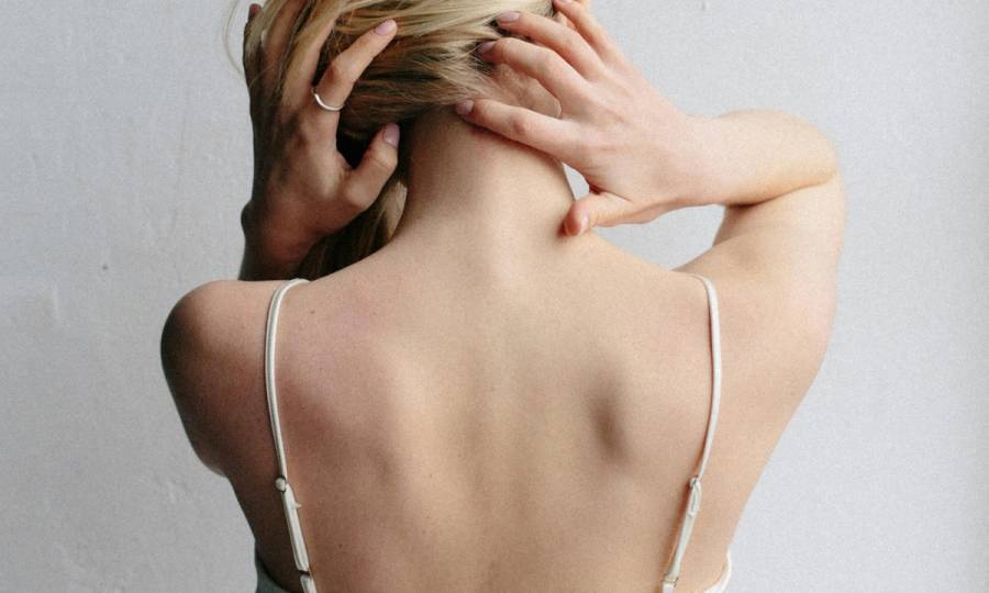 back view of woman in tank top holding her hair and neck