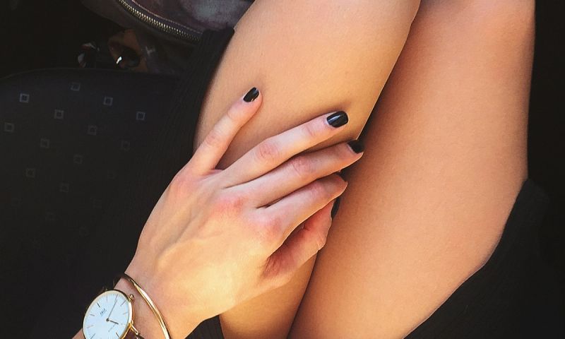 hand with dark nail polish manicure resting on thigh