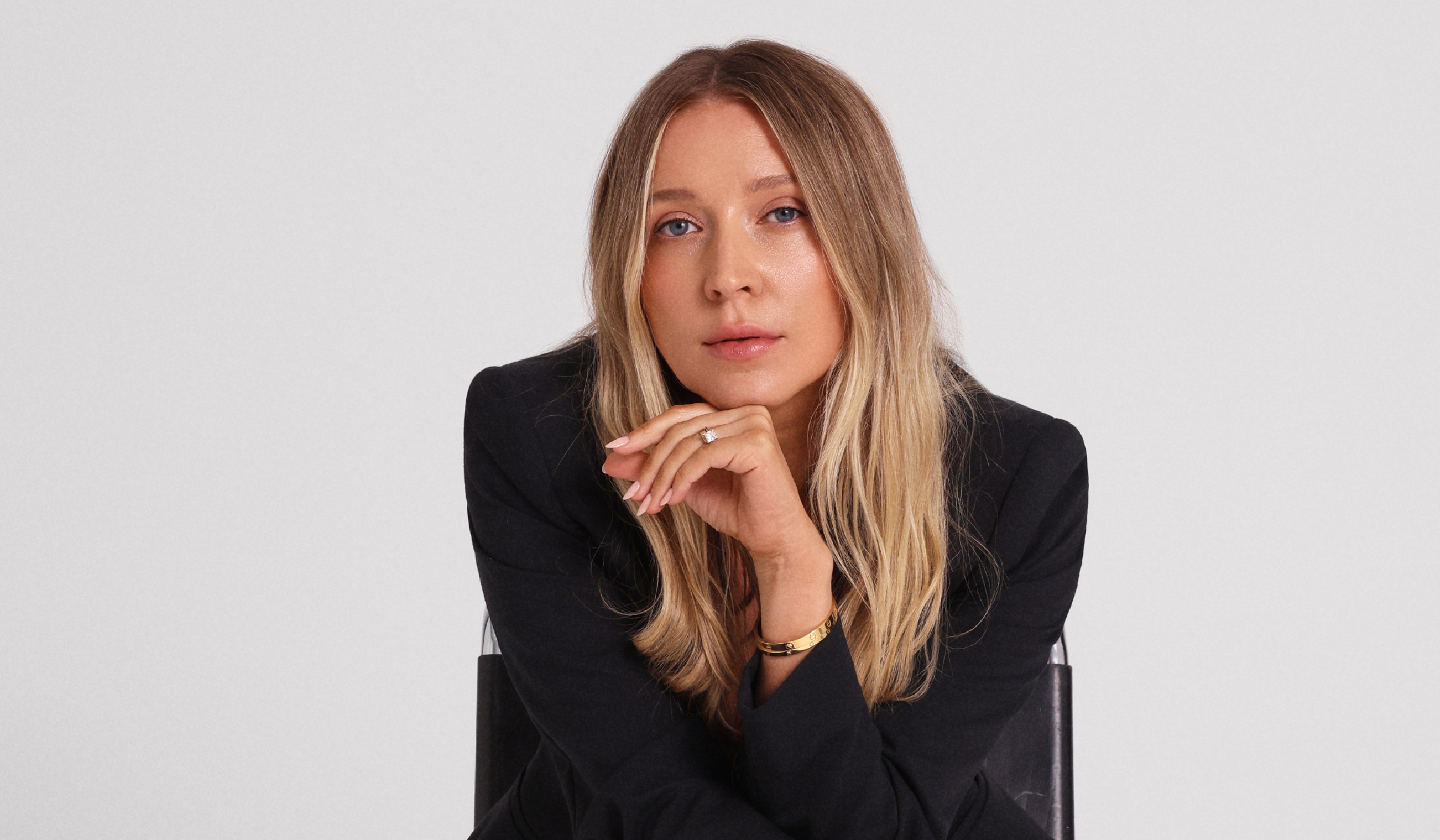 Margarita Nazarenko sits in a black chair wearing a black blazer, resting her chin on her hand.