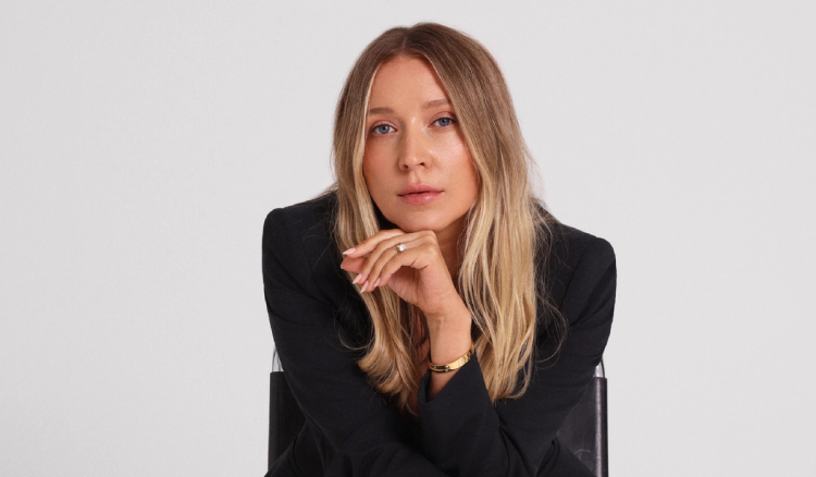 Margarita Nazarenko sits in a black chair wearing a black blazer, resting her chin on her hand.