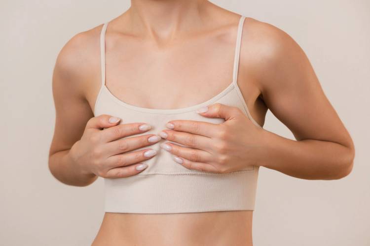  young woman in beige underwear holds her small breasts with both hands isolated on a beige background. 