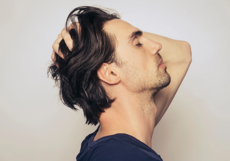 Profile of a man with thick, dark hair, eyes closed, running both hands through his hair