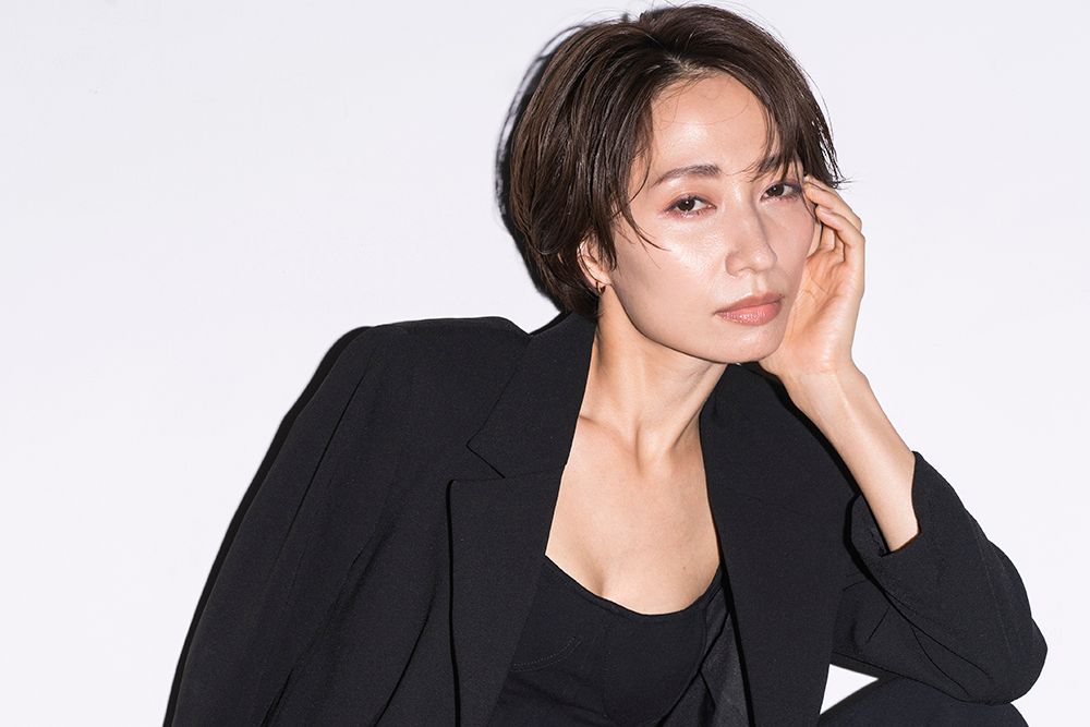 An Asian woman with beautiful skin and wet styled hair is posing sideways. Studio shot on white background. Dressed in black.