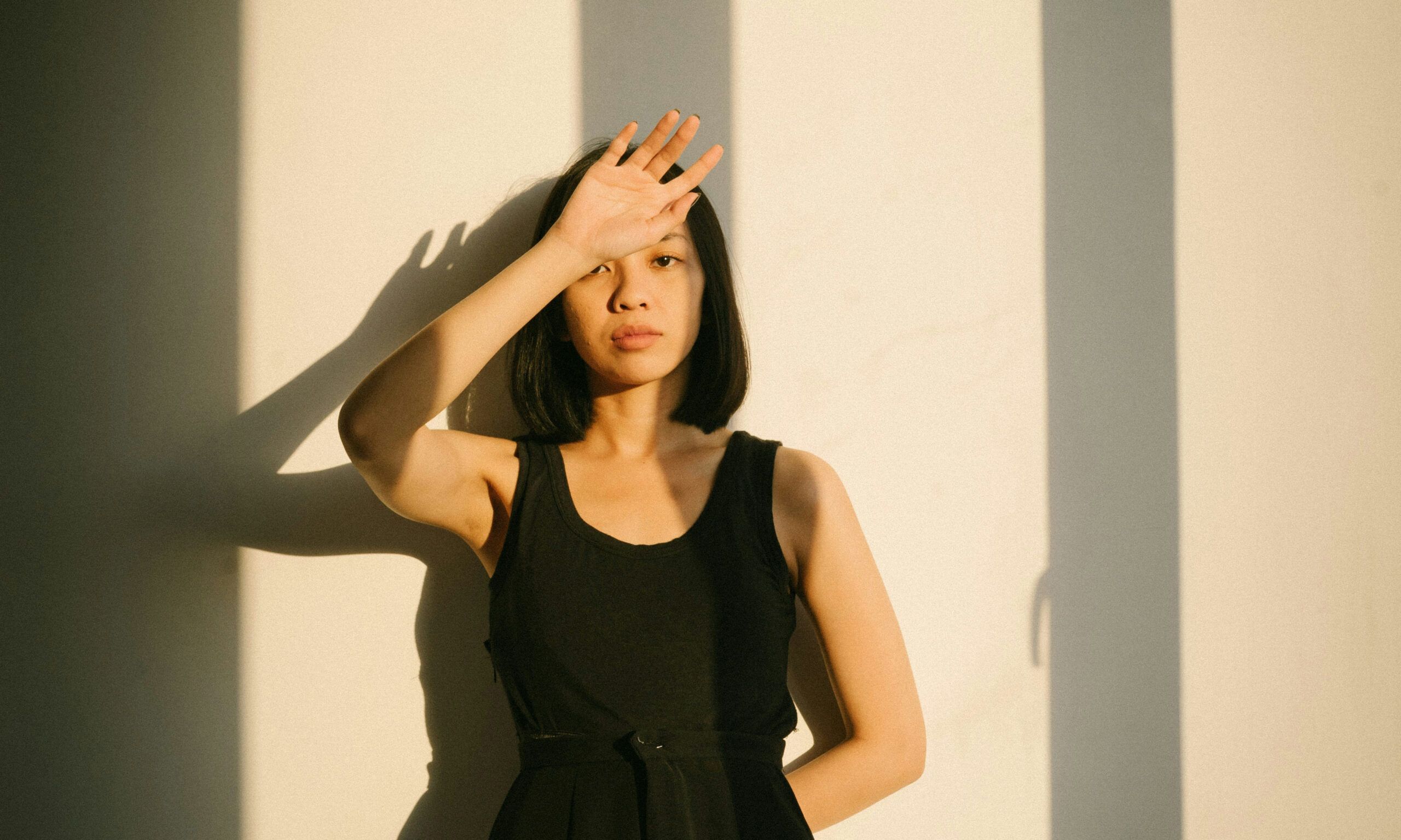 Asian woman in black dress standing in sunset shadows with hand in front of face