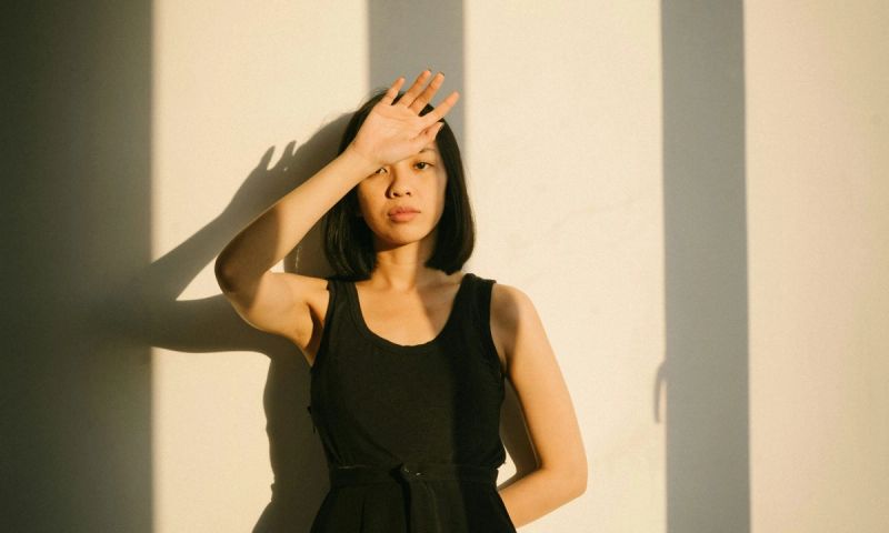 Asian woman in black dress standing in sunset shadows with hand in front of face