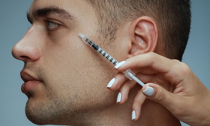 Close-up profile portrait of young man isolated on grey studio background. Filling botox surgery procedure. Concept of men's health and beauty, cosmetology, self-care, body and skin care. Anti-aging.