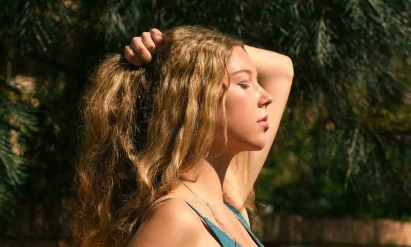 Woman holding up blonde wavy hair in the sunshine