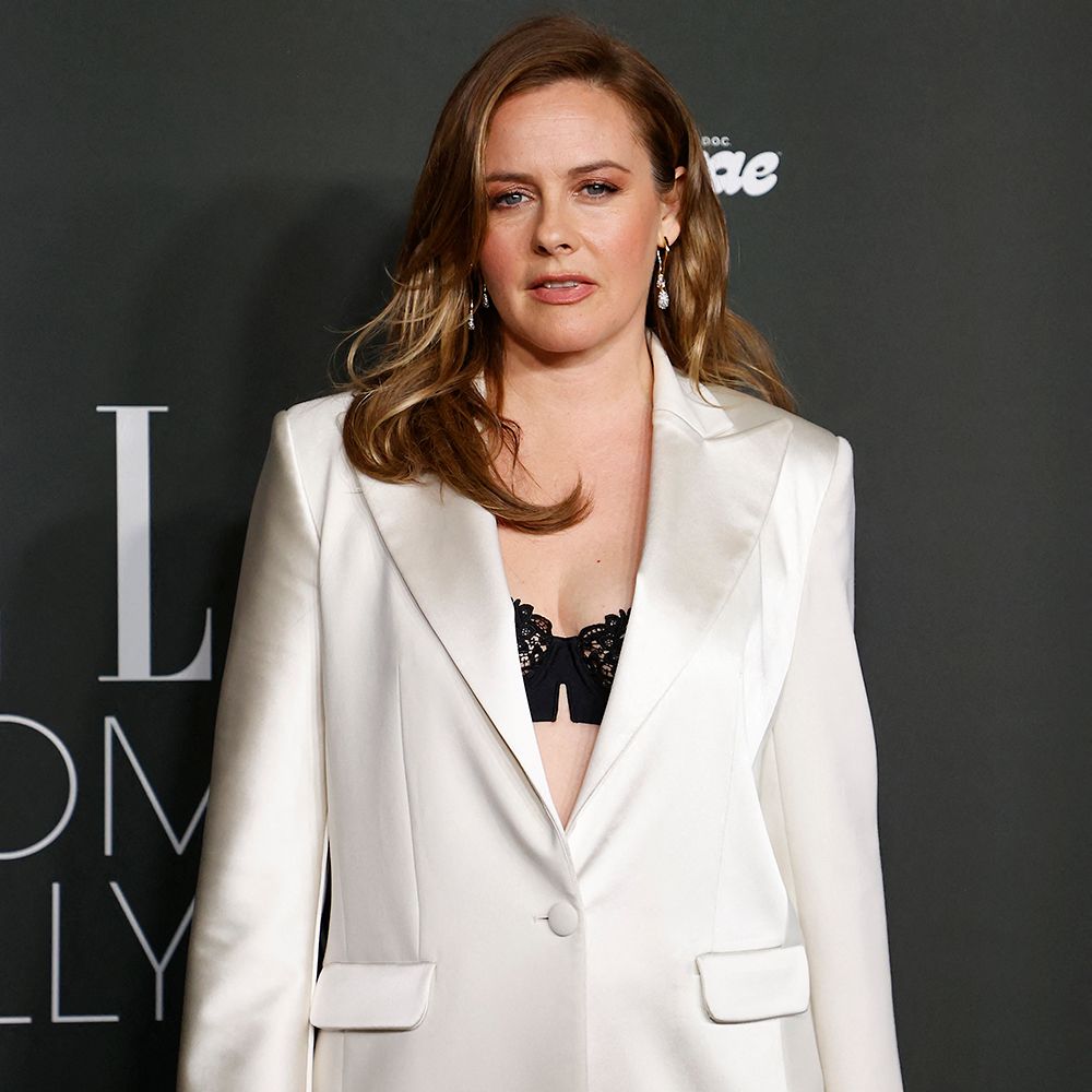 Alicia Silverstone poses on the red carpet in a white suit and black bra