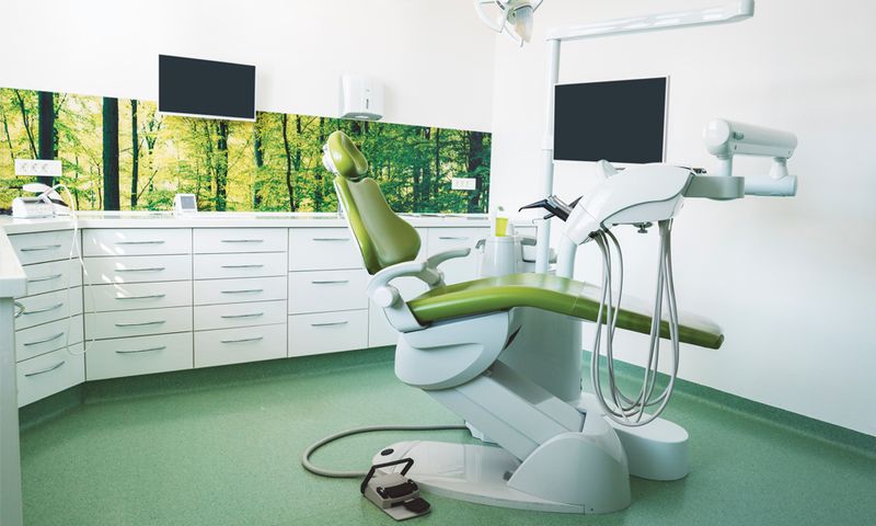 Empty brightly lit place of work of a dentist, modern dentist office with green dentist's chair, no people
