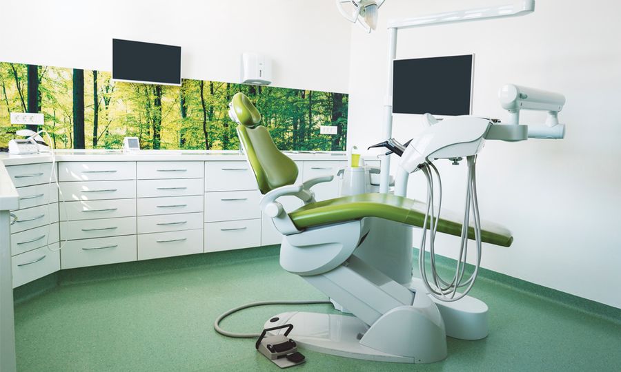 Empty brightly lit place of work of a dentist, modern dentist office with green dentist's chair, no people