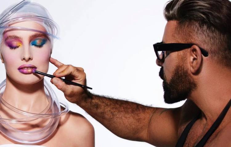 Scott Barnes applies lip color to a model wearing bold, colorful makeup during a studio beauty shoot.