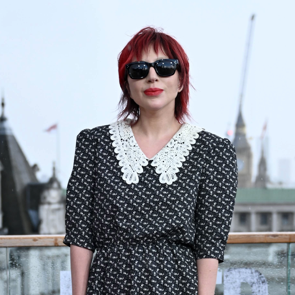 A photo of Lady Gaga with a short haircut and red hair as she stands outside with a cityscape behind her