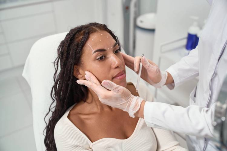 A practitioner in gloves marks a patient's face before an aesthetic treatment