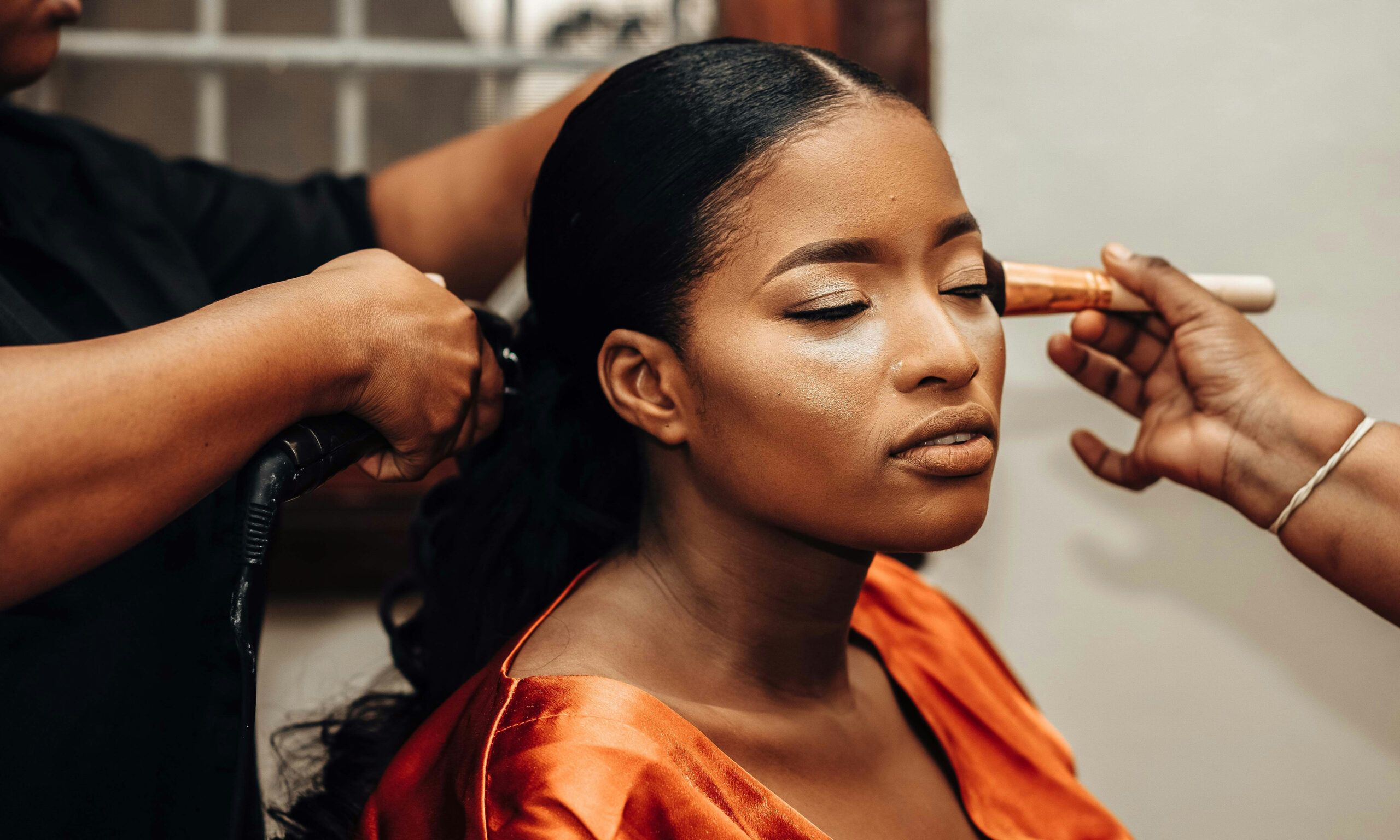 Black woman getting her hair and makeup done by professionals