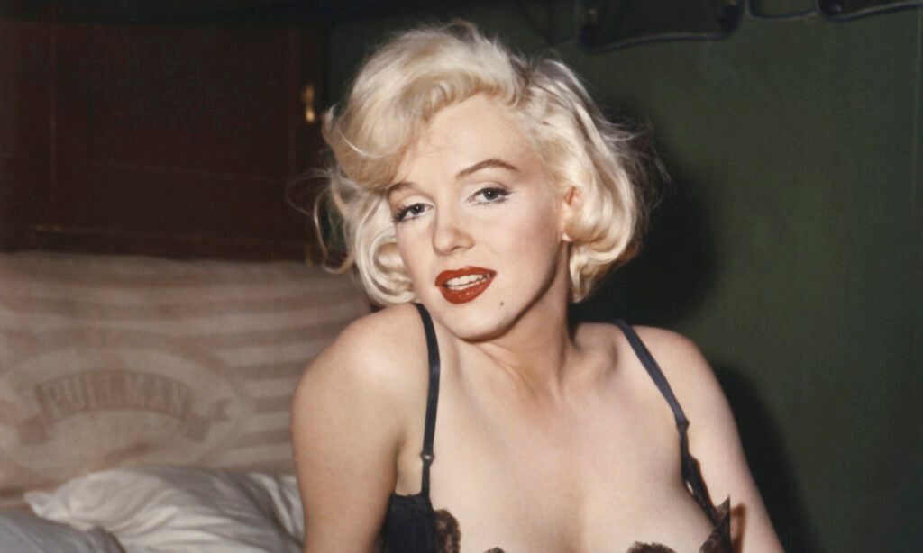 Marilyn Monroe wearing low cut black slip sitting up in train bunk bed from the 1959 Billy Wilder film 'Some Like It Hot'.