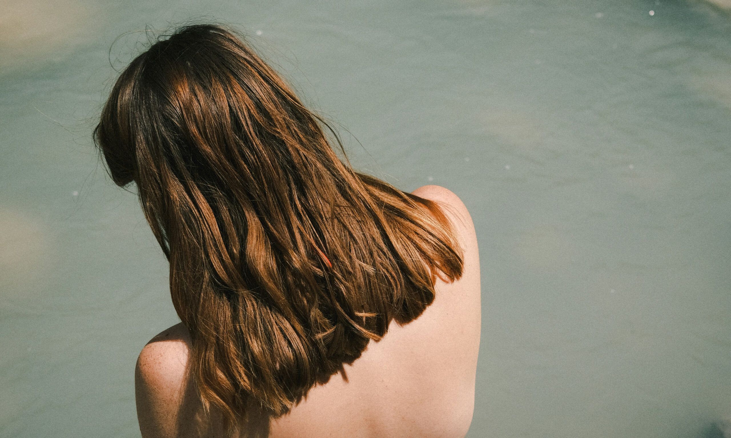 back view of woman with brown hair sitting on dock