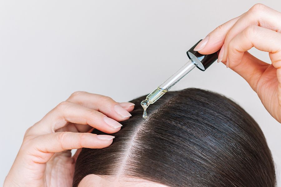 Close-up young brunette woman applying a drop of oil from pipette to her scalp. Hair loss. Strengthening and growth of hair. Hair care.