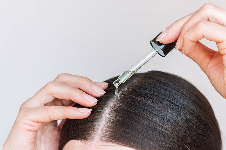 Close-up young brunette woman applying a drop of oil from pipette to her scalp. Hair loss. Strengthening and growth of hair. Hair care.