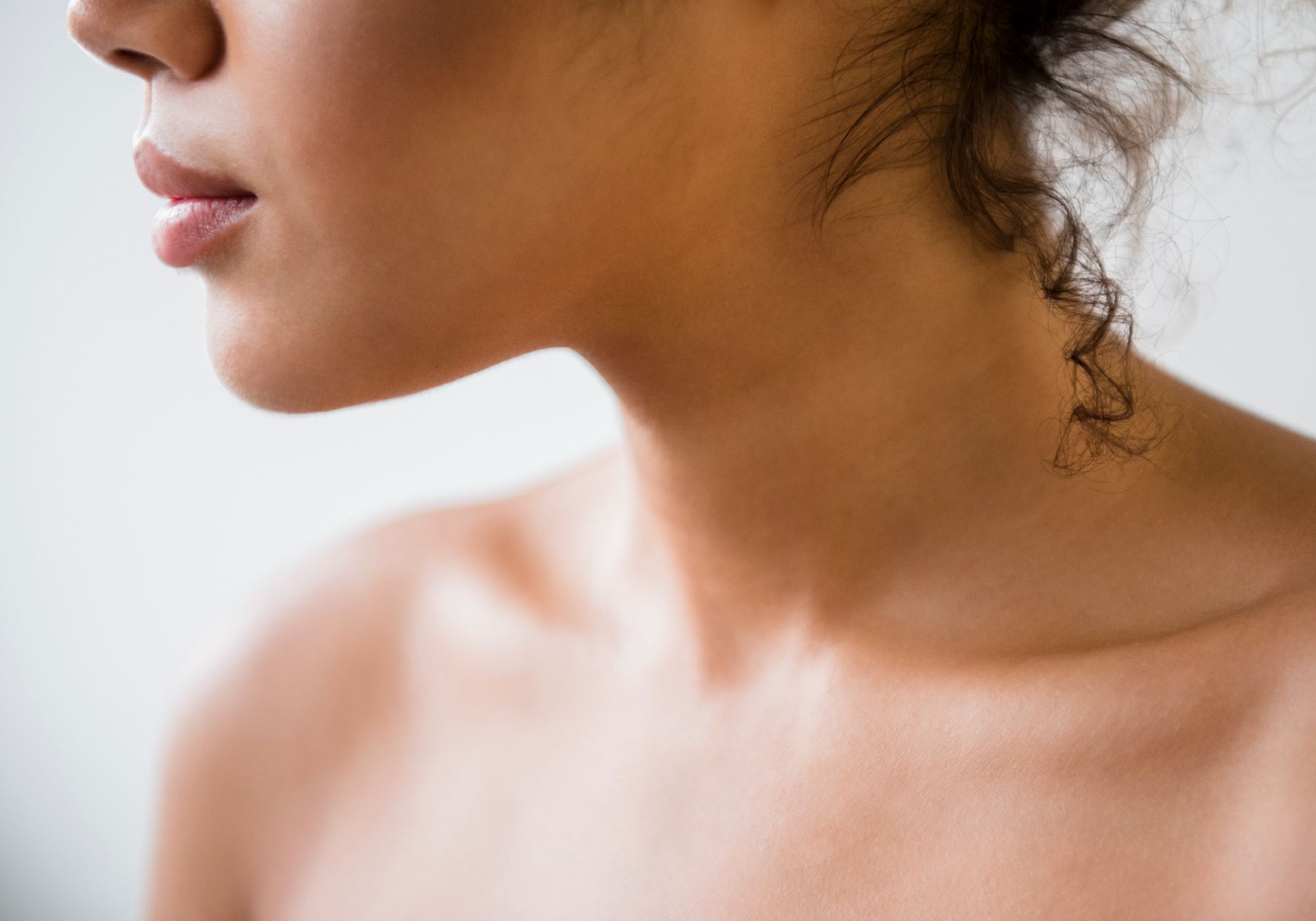 Close-up profile of a woman's neck and décolletage against a light gray background.