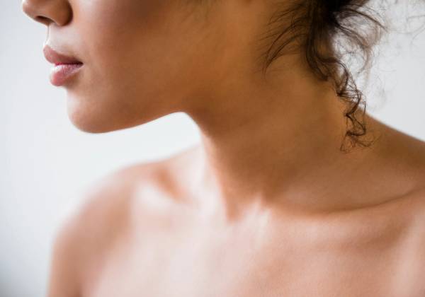 Close-up profile of a woman's neck and décolletage against a light gray background.