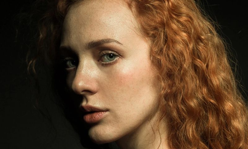 A portrait of a red and curly-haired woman on a black background