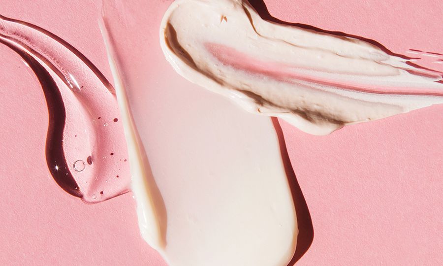 Textured multi colored smears of cosmetics on pink background. Samples of creams, face mask, face gel, serum. Flat lay, top view.
