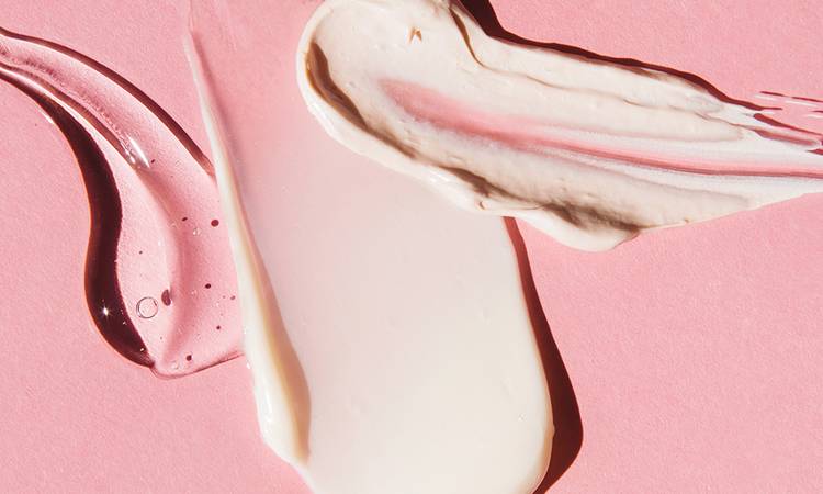 Textured multi colored smears of cosmetics on pink background. Samples of creams, face mask, face gel, serum. Flat lay, top view.