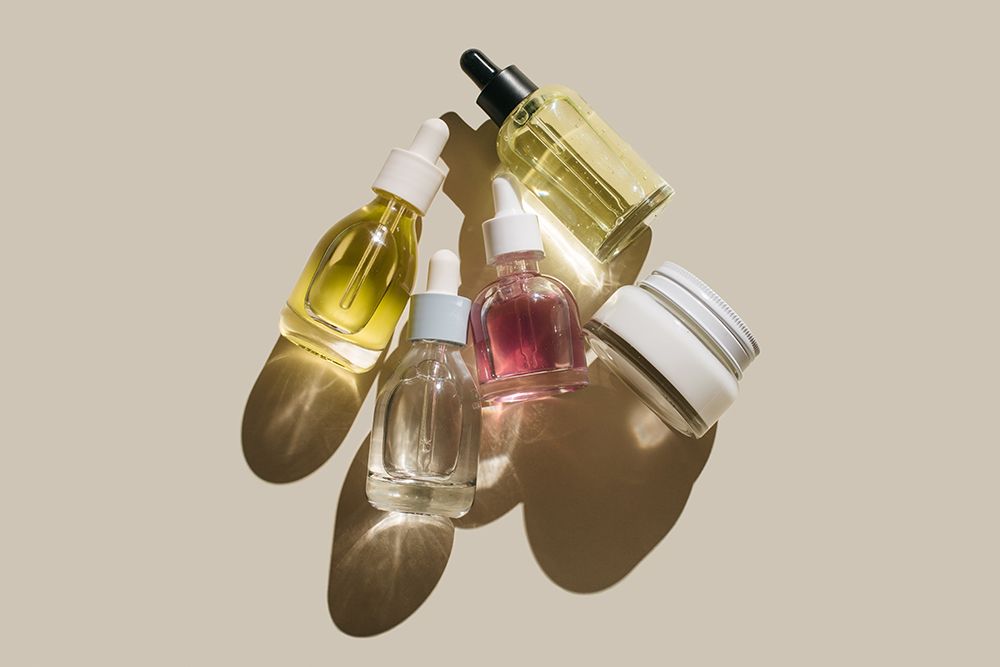Glass bottles for cosmetic products with pipette, natural skincare face cream and essential oil on beige background. Beauty products. Multitasking beauty, skinmalism, Skin care concept.
