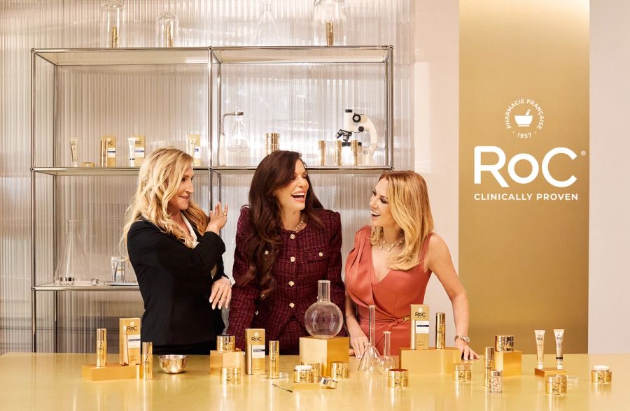 Bethenny Frankel, Sonja Morgan and Ramona Singer pose together at a lab-style setup surrounded by RoC skin-care products during their campaign shoot.