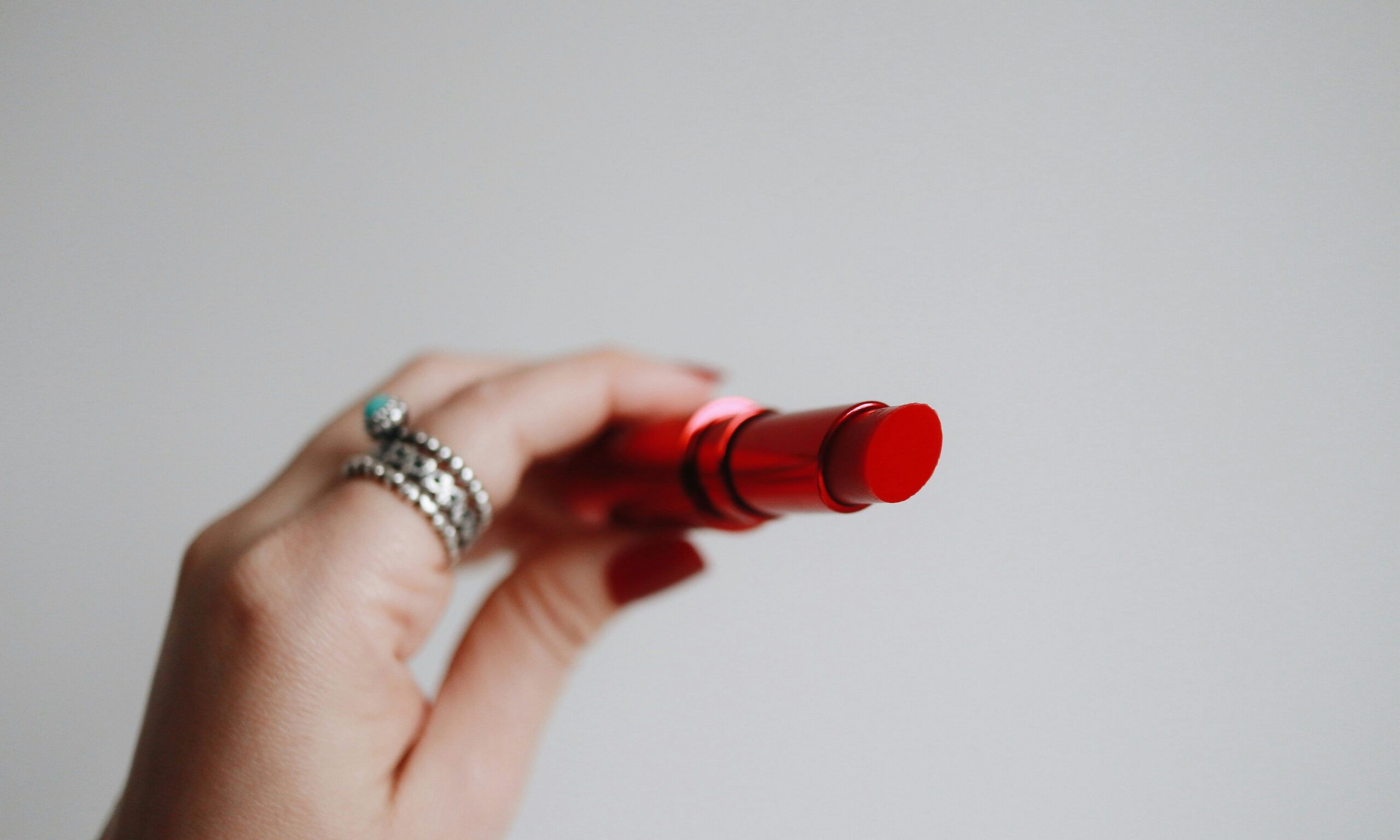 hand holding an open red lipstick against a gray background