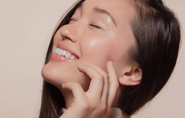 Smiling woman with glowing, dewy skin touching her cheek with her fingertips