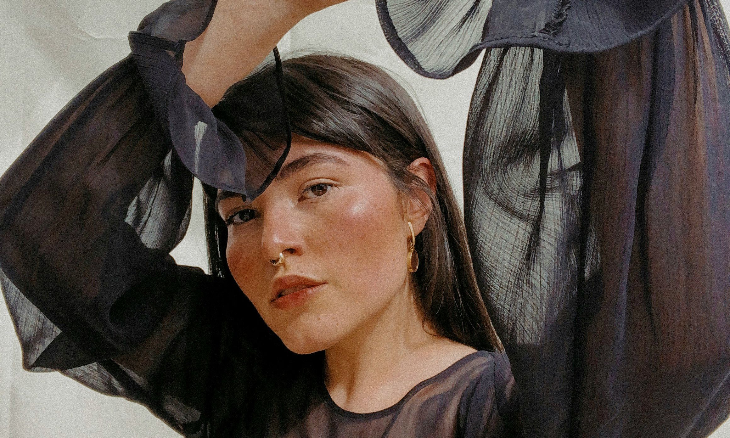 woman with pretty makeup with dark hair wearing a sheer black blouse with hands above her head