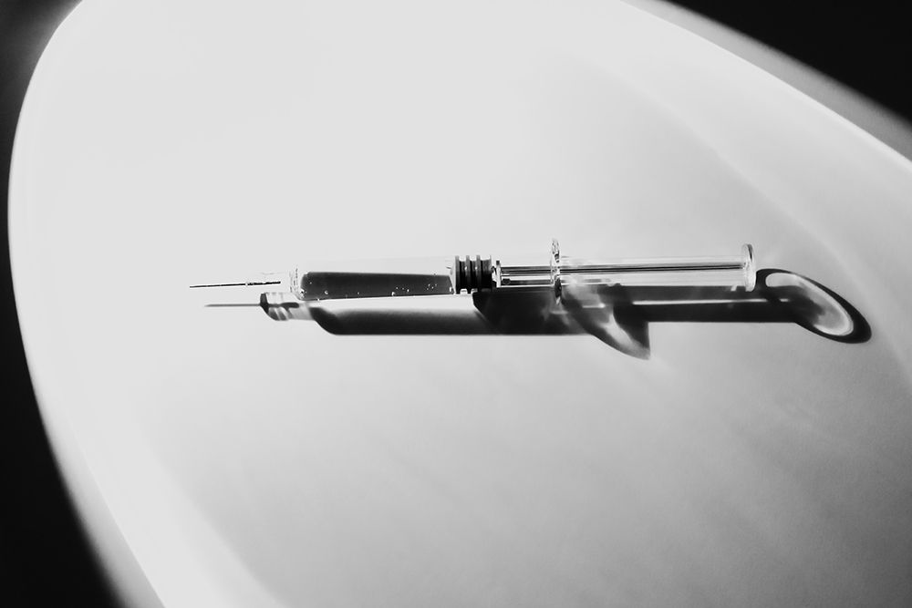 Syringe on white background with distinct shadow falling from side. dramatic mood. Use in medical or pharmaceutical contexts, illustrations of articles, presentations, marketing materials relating to medicine, vaccination, treatment or medical research.