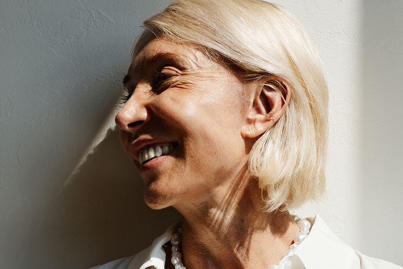 Minimal side view portrait of elegant mature woman lit by sunlight against white wall