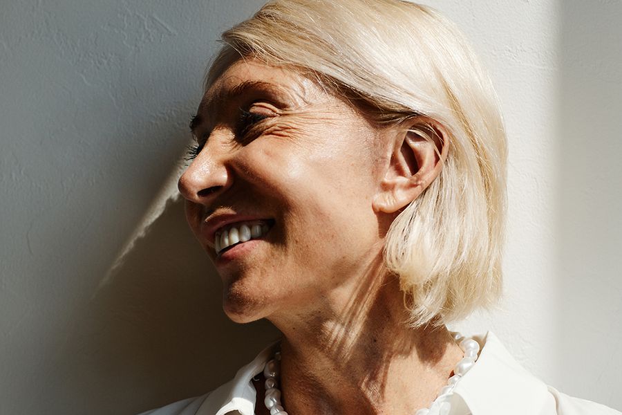 Minimal side view portrait of elegant mature woman lit by sunlight against white wall