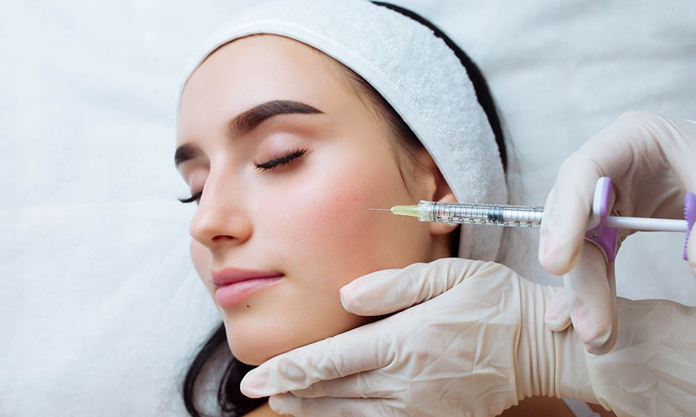 Smile lifting and lip augmentation. Beautician doctor hands doing beauty procedure to female face with syringe. Young woman's mouth contouring with filler injection. Marionette lines treatment.