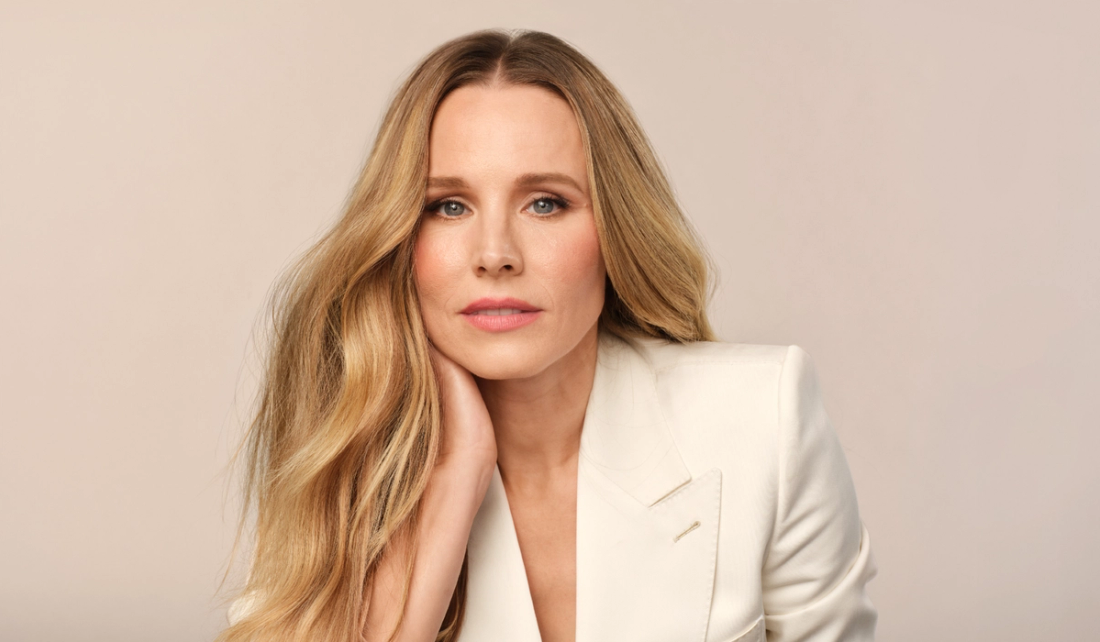 Kristen Bell poses with long wavy blonde hair, wearing a cream blazer against a neutral beige background