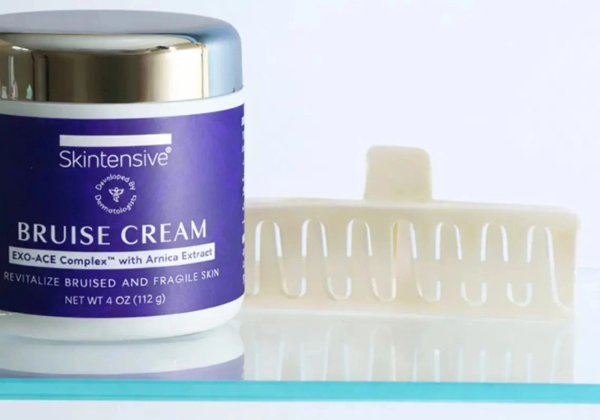 A jar of Skintensive Bruise Cream with EXO-ACE Complex and arnica extract next to a white hair claw clip on a glass shelf.