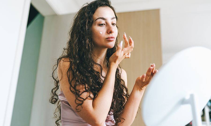 Priming skin: woman uses base cream and foundation in front of mirror. Preparing for the spotlight with skincare and makeup.