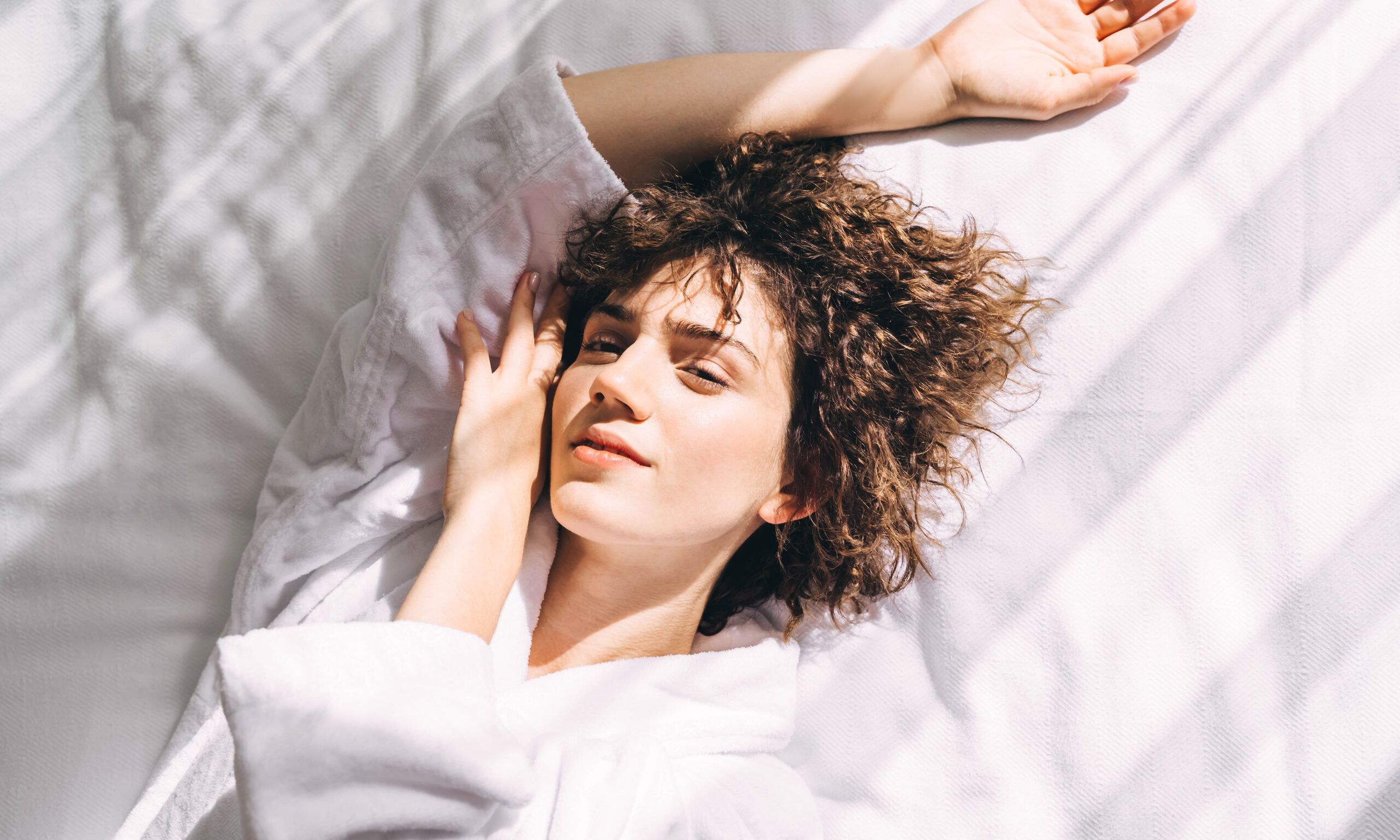 Woman in a white terry bathrobe on the bed in the morning, top view.