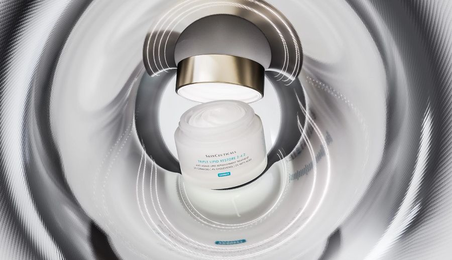 Woman applying moisturizer to her face in front of a mirror, illustrating a barrier-supporting skin-care routine to reduce retinoid irritation and support healthy skin.