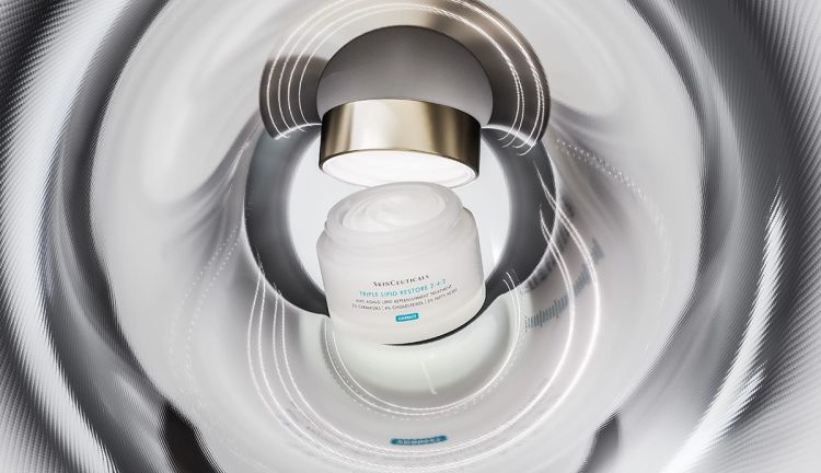 Woman applying moisturizer to her face in front of a mirror, illustrating a barrier-supporting skin-care routine to reduce retinoid irritation and support healthy skin.