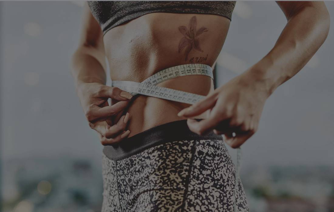 Close-up of a woman in workout clothes wrapping a measuring tape around her waist.