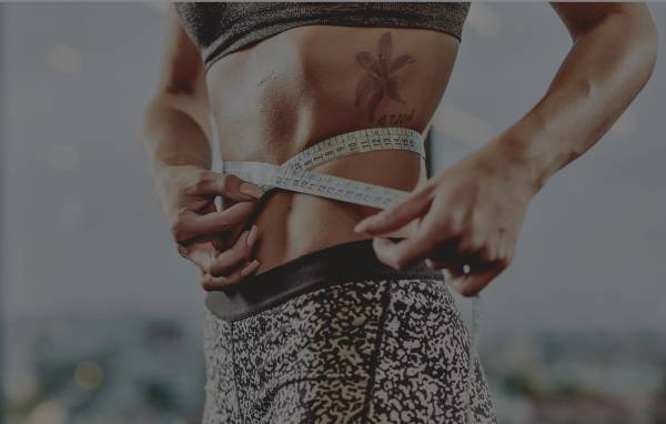 Close-up of a woman in workout clothes wrapping a measuring tape around her waist.