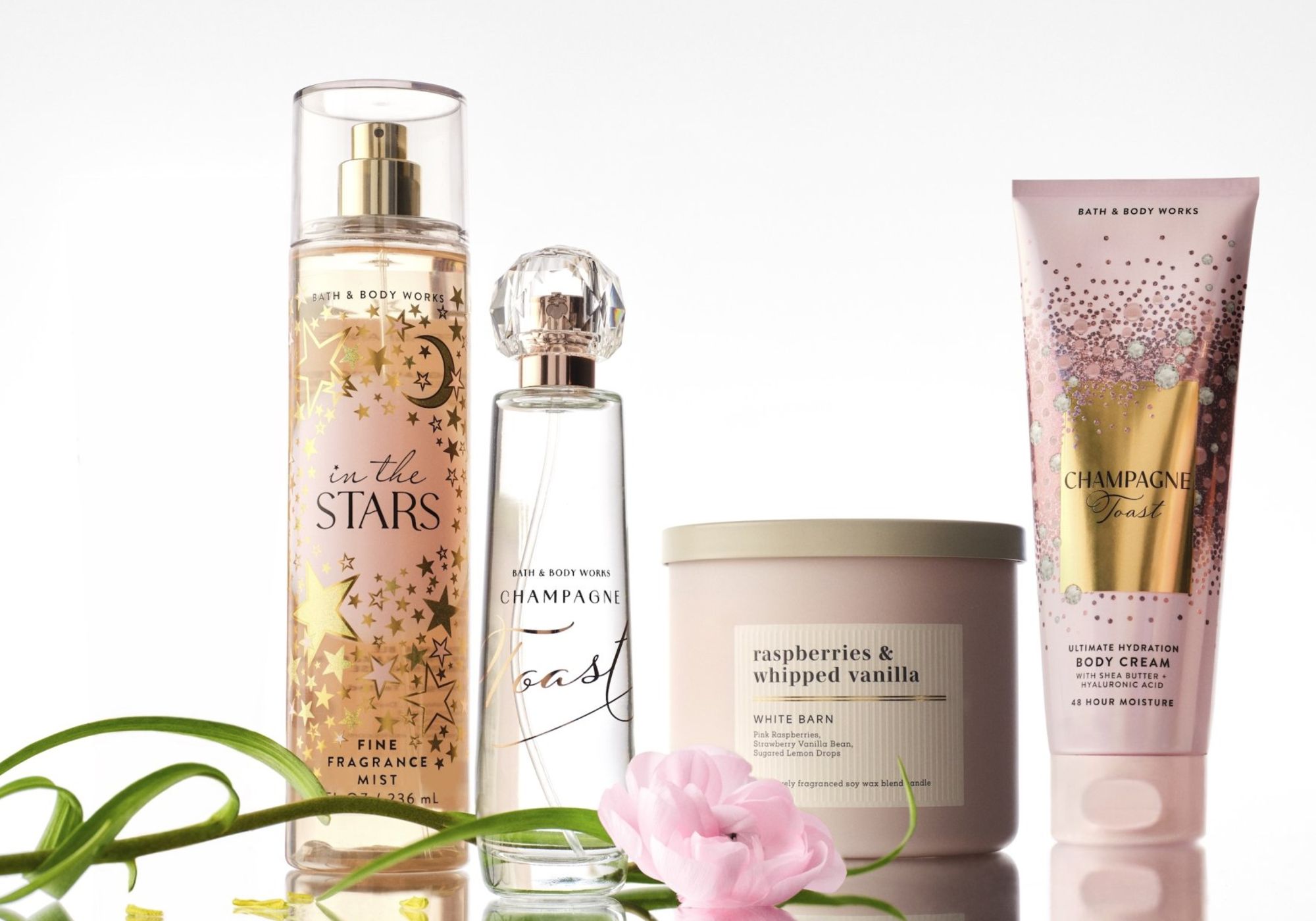 Bath & Body Works fragrance mist, perfume, candle and body cream products arranged with a pink flower on a white background