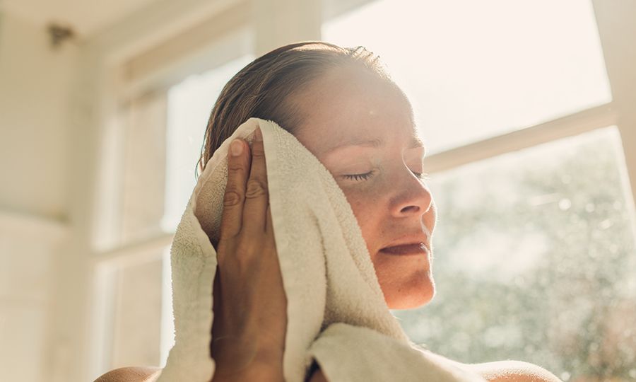 Woman toweling oneself off after bathing in sunny bathroom.