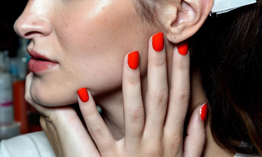 close view of hand with red nail polish on nails on woman's own face