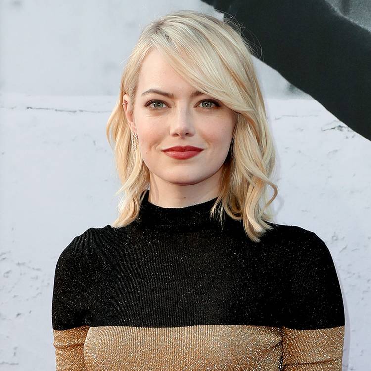 Emma Stone with blonde hair wearing a gold and black turtleneck