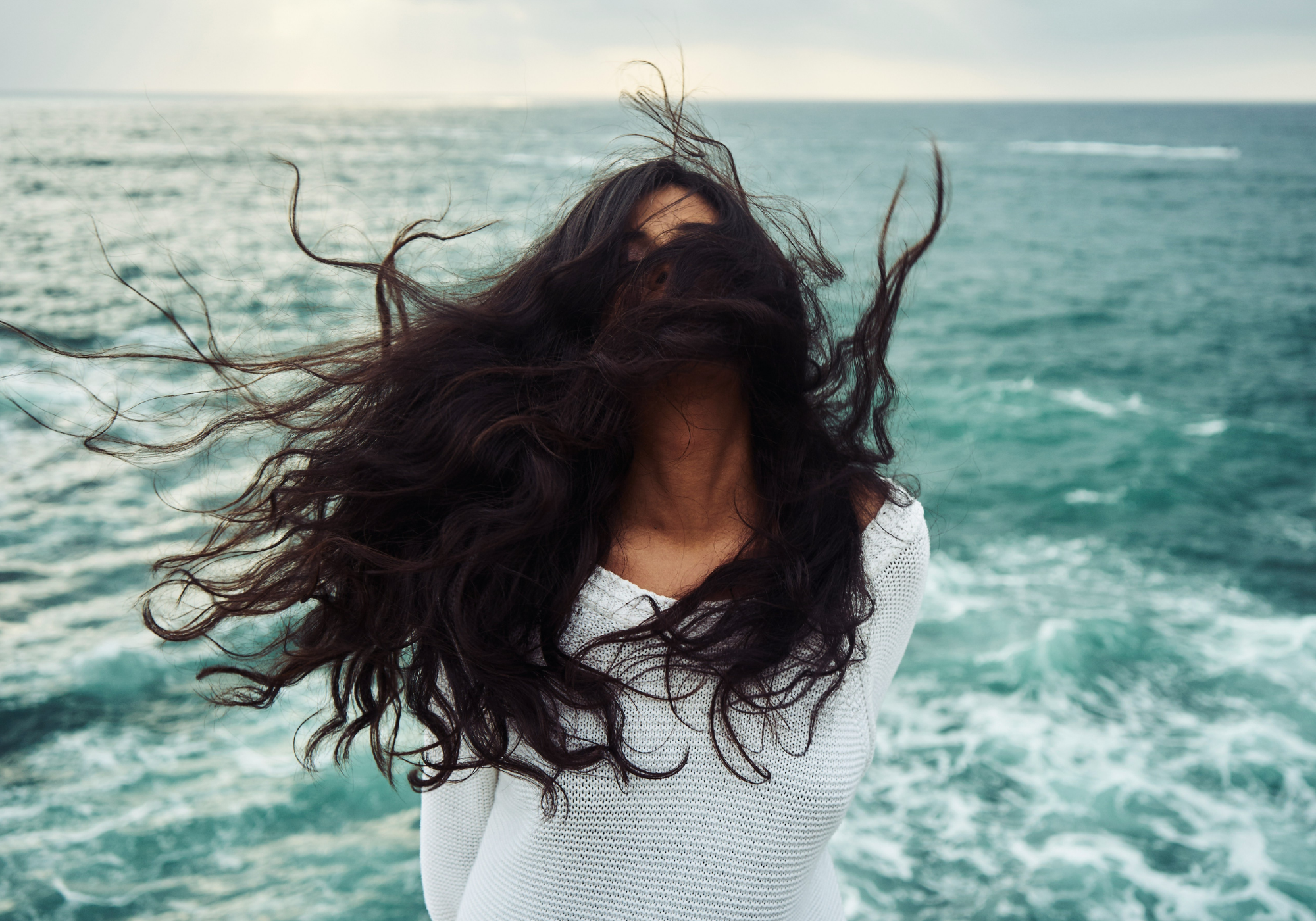 Windblown hair by the ocean illustrating frizzy hair caused by humidity and moisture